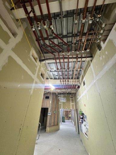 Overhead pipework and supports along a corridor under construction.