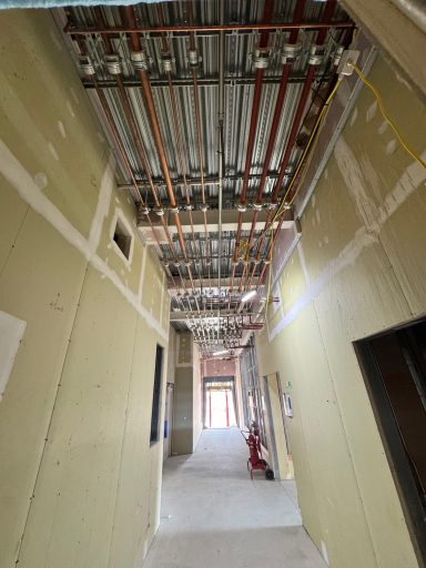 Multiple parallel pipework runs above an unfinished corridor.
